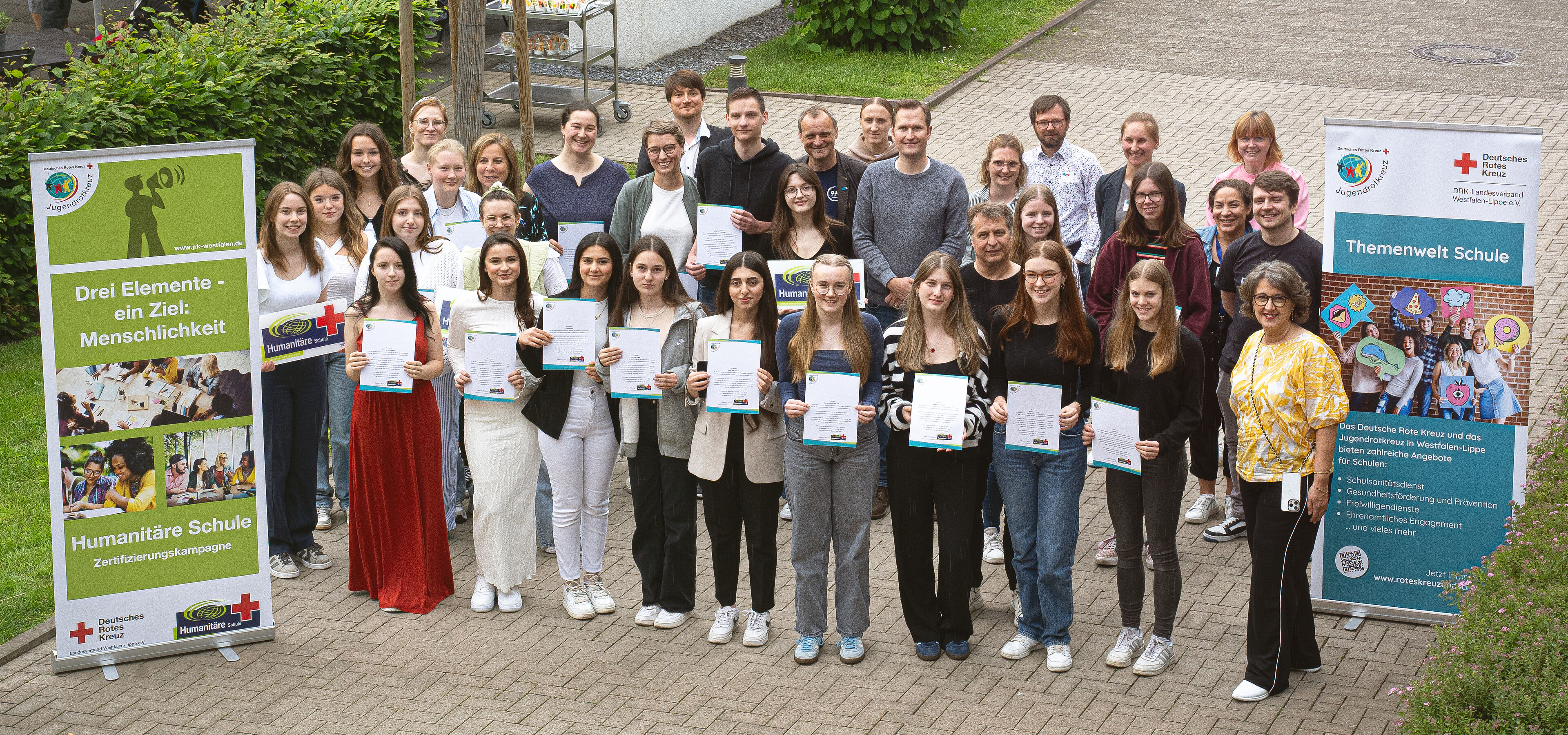 Gruppenbild der Teilnehmer mit ihren Zertifikaten zwischen zwei Roll-Ups.