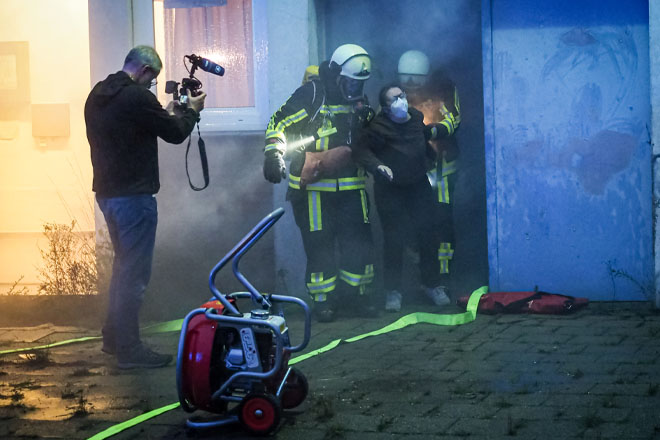 Zwei Feuerwehrleute bringen eine verletzte Frau aus einem verrauchten Gebäude. 