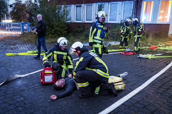 Zwei Feuerwehrleute kümmern sich um einen Verletzten Mann am Boden.