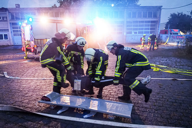 Vier Feuerwehrleute legen einen Mann auf eine Trage.