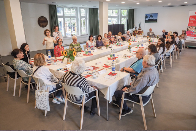 Junge und alte Menschen sitzen an einer Kaffeetafel.