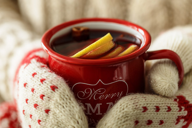 Zwei Hände mit gestrickten Handschuhen halten eine Tasse mit Glühwein.